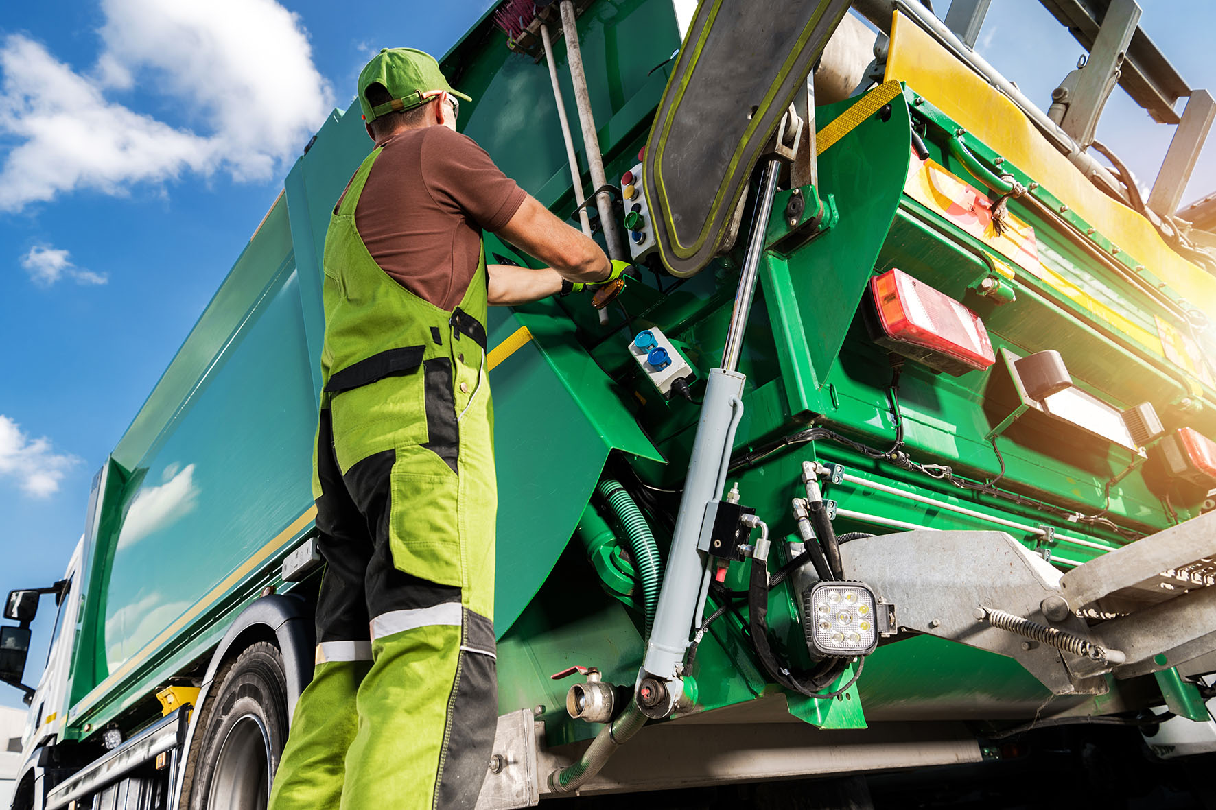 Waste Collection Worker Operating Garbage Truck Worker in high-visibility clothing operating a green garbage truck during waste collection.