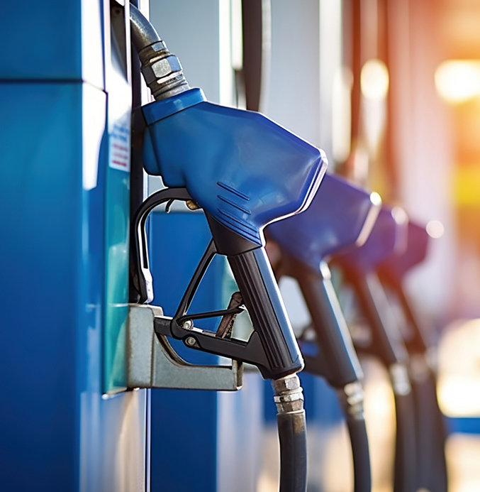 Close-up of blue fuel pump nozzles at a gas station with sunlight in the background.