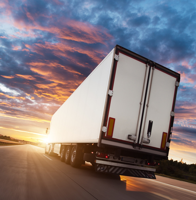 Truck driving on a highway at sunset with a dramatic sky in the background.