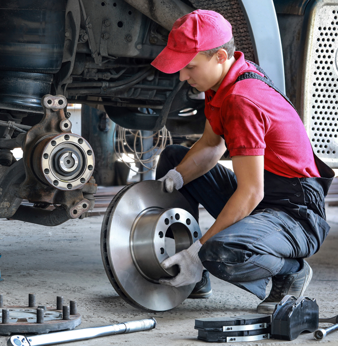 Mechanic installing a brake disc on a truck axle in a workshop, with tools and brake components on the floor.