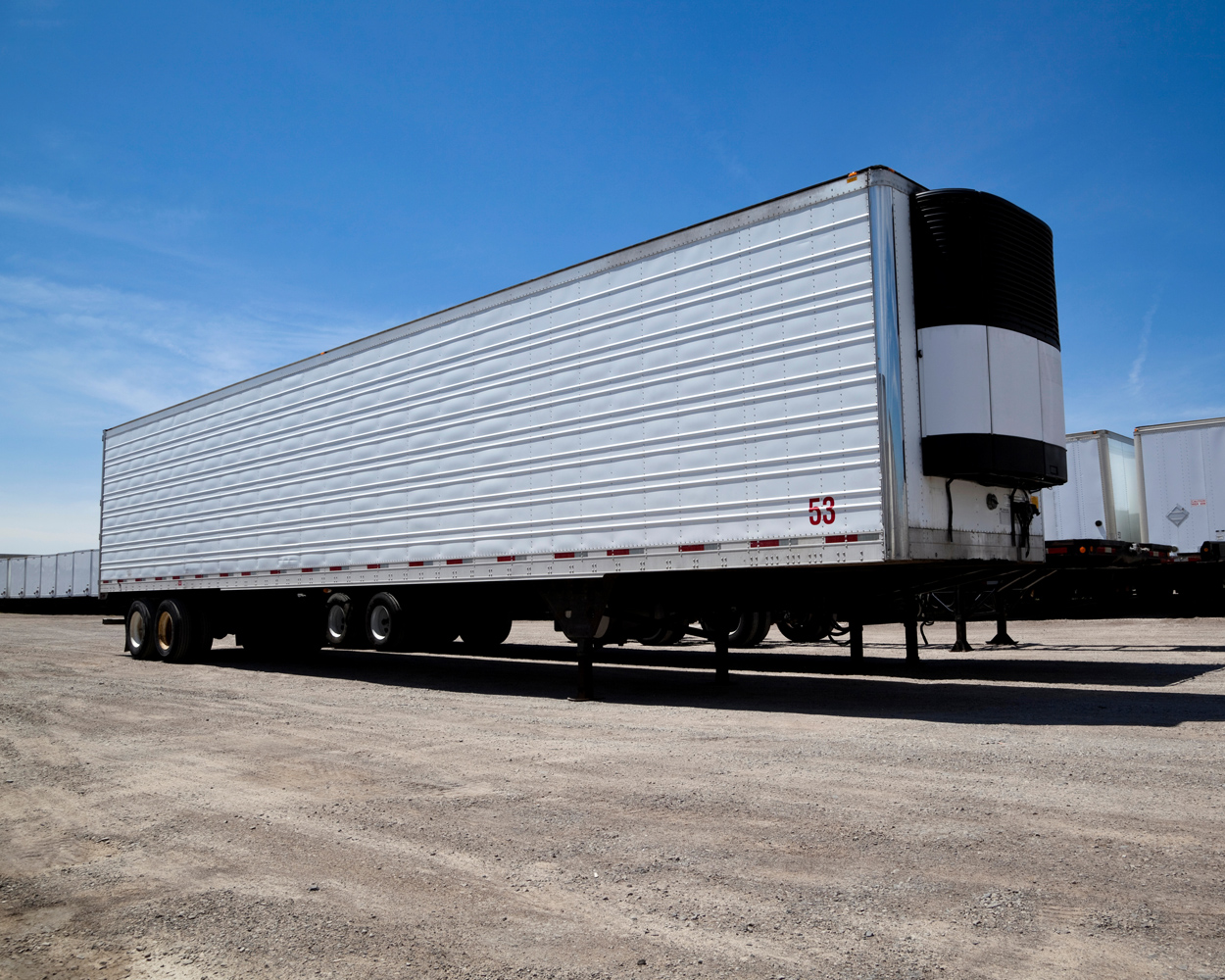 Large refrigerated semi-trailer parked in a logistics yard under a clear blue sky.