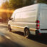 White delivery van driving through a city street at sunset, with motion blur and warm sunlight highlighting speed, efficiency, and modern logistics operations.
