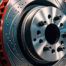 Close-up of a high-performance ventilated and drilled brake disc with red brake caliper components in an automotive workshop setting.
