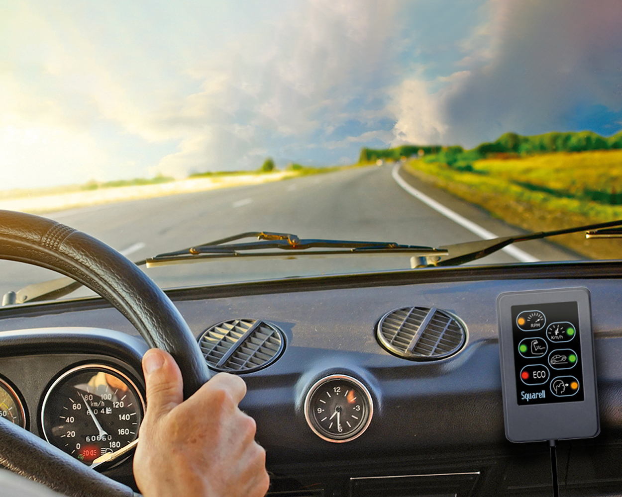 DAP on truck dashboard Driver’s view from inside a vehicle, showing a hand on the steering wheel, the dashboard, and a DAP device mounted beside the instruments while driving on an open road.
