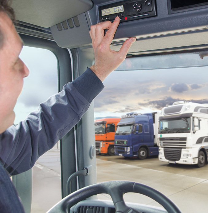 Truck Driver Using a Digital Tachograph Truck driver operating a digital tachograph inside a truck cab, with several parked trucks visible outside.