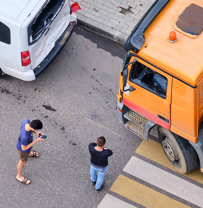 Aerial view of a traffic accident involving an orange construction truck and a white van near a pedestrian crossing, with two people inspecting the scene.