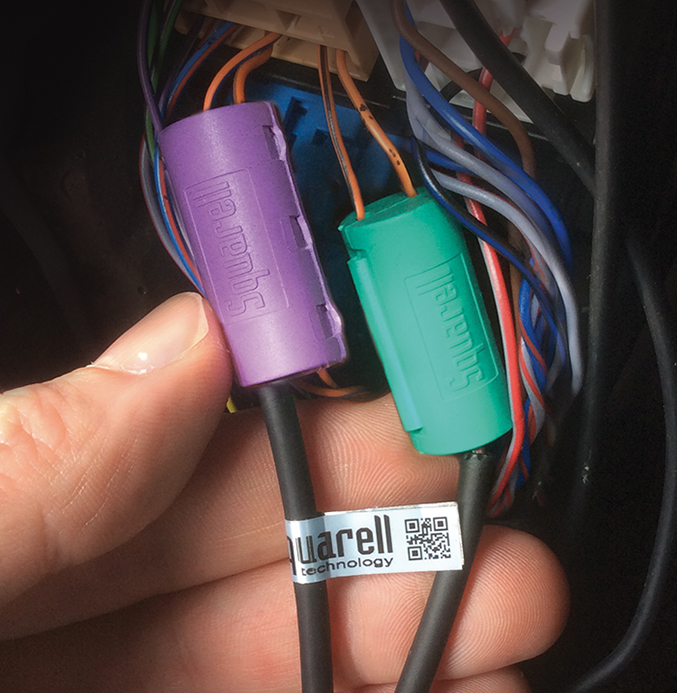 CANcliQ and DatacliQ in Vehicle Wiring Harness Close-up of a hand holding two colored DatacliQ and CANcliQ connectors (purple and green) attached to wiring inside a vehicle.