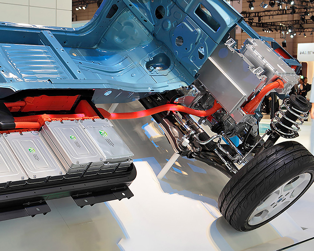Electric vehicle chassis showing an underfloor battery pack, high-voltage cables, electric drive unit, and front suspension components.