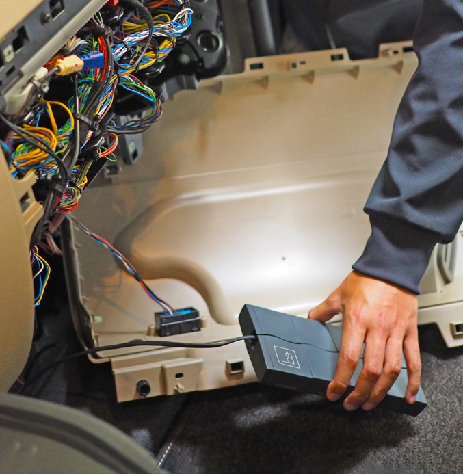 Installing a BE device Technician installing a BE vehicle telematics device beneath the dashboard of a commercial vehicle.