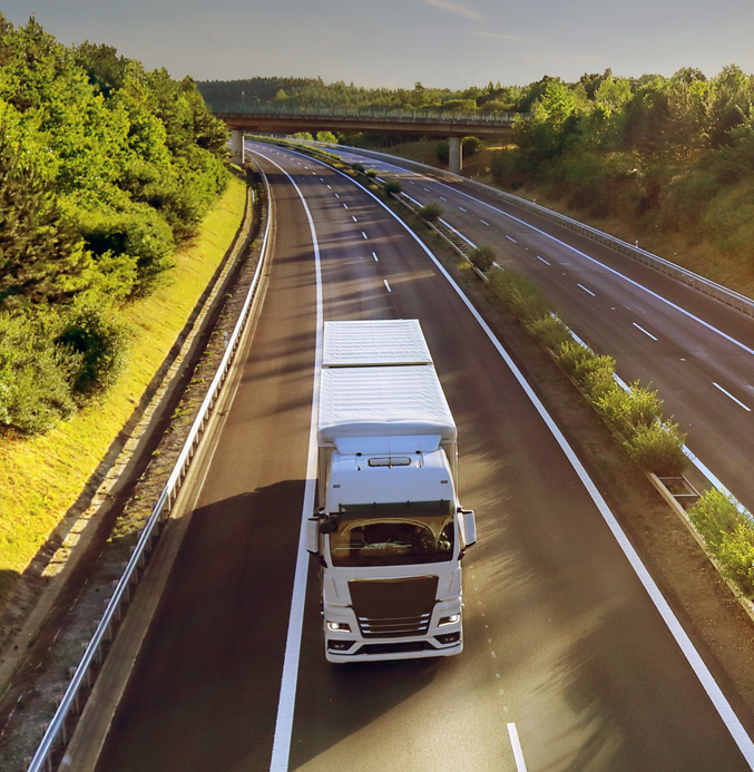 White Semi-Truck Transporting Goods on a Scenic Highway White semi-truck driving on a modern highway surrounded by green forests during golden hour.