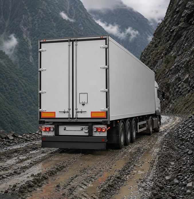 White Semi-Truck on a Rough Mountain Road Rear view of a clean white semi-trailer truck driving along a severely muddy and rutted mountain road.