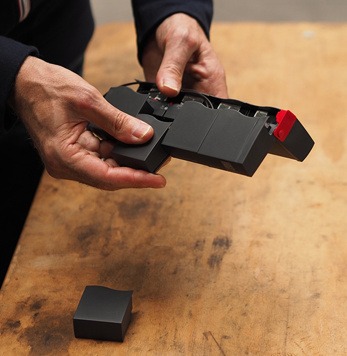 Modular Data Interface Being Handled Hands holding and inspecting a black modular data interface device with red components above a wooden workbench.