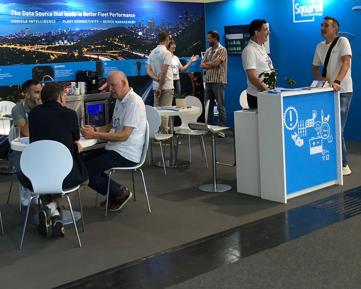 Visitors and representatives networking at the Squarell Technology exhibition booth, showcasing vehicle intelligence, fleet connectivity, and device management solutions.